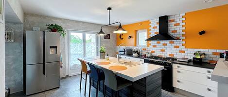 A modern kitchen with a central island, stainless steel appliances, and a bright orange accent wall.