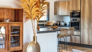 A modern kitchen with wooden cabinets, a central island with bar stools, and a vase with pampas grass.
