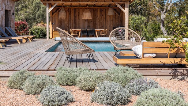 A wooden deck with a pool, lounge chairs, and a covered seating area.