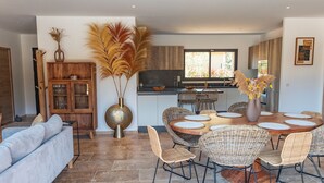 A modern living room with a sofa, dining table with chairs, and a kitchen area with a window.