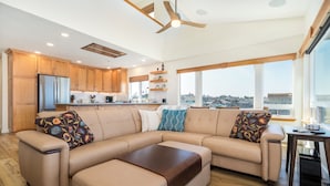 A modern living room with a beige sectional sofa, wooden flooring, a ceiling fan, and a view of the city through large windows. - Experience Nature's Spectacle from the Front Row! (Newport)