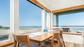 A dining area with a wooden table and chairs, large windows with a view of the beach and ocean, and a wooden ceiling. - Experience Nature's Spectacle from the Front Row! (Newport)