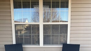 Two black wicker chairs with cushions, a small black table with a potted plant, and a window with blinds.