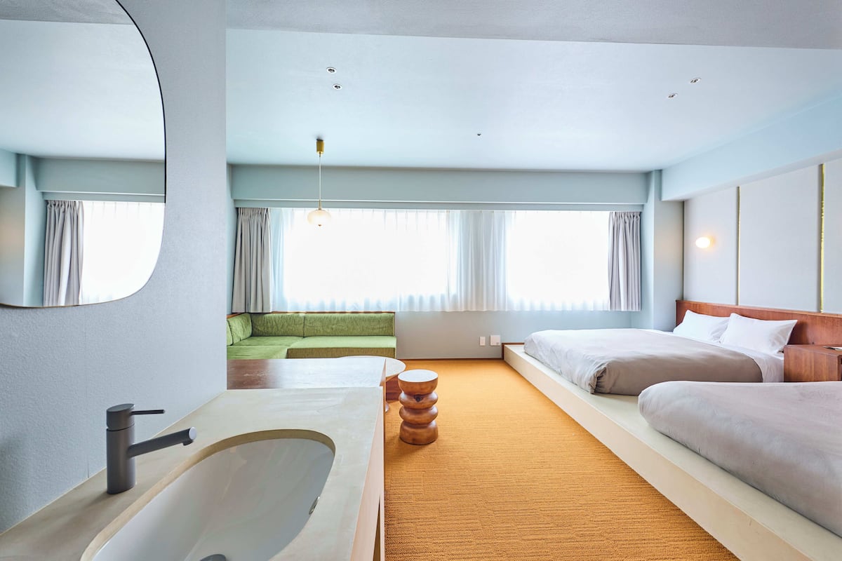 A modern hotel room with a large bathtub, a sofa, a bed, and a round wooden table.