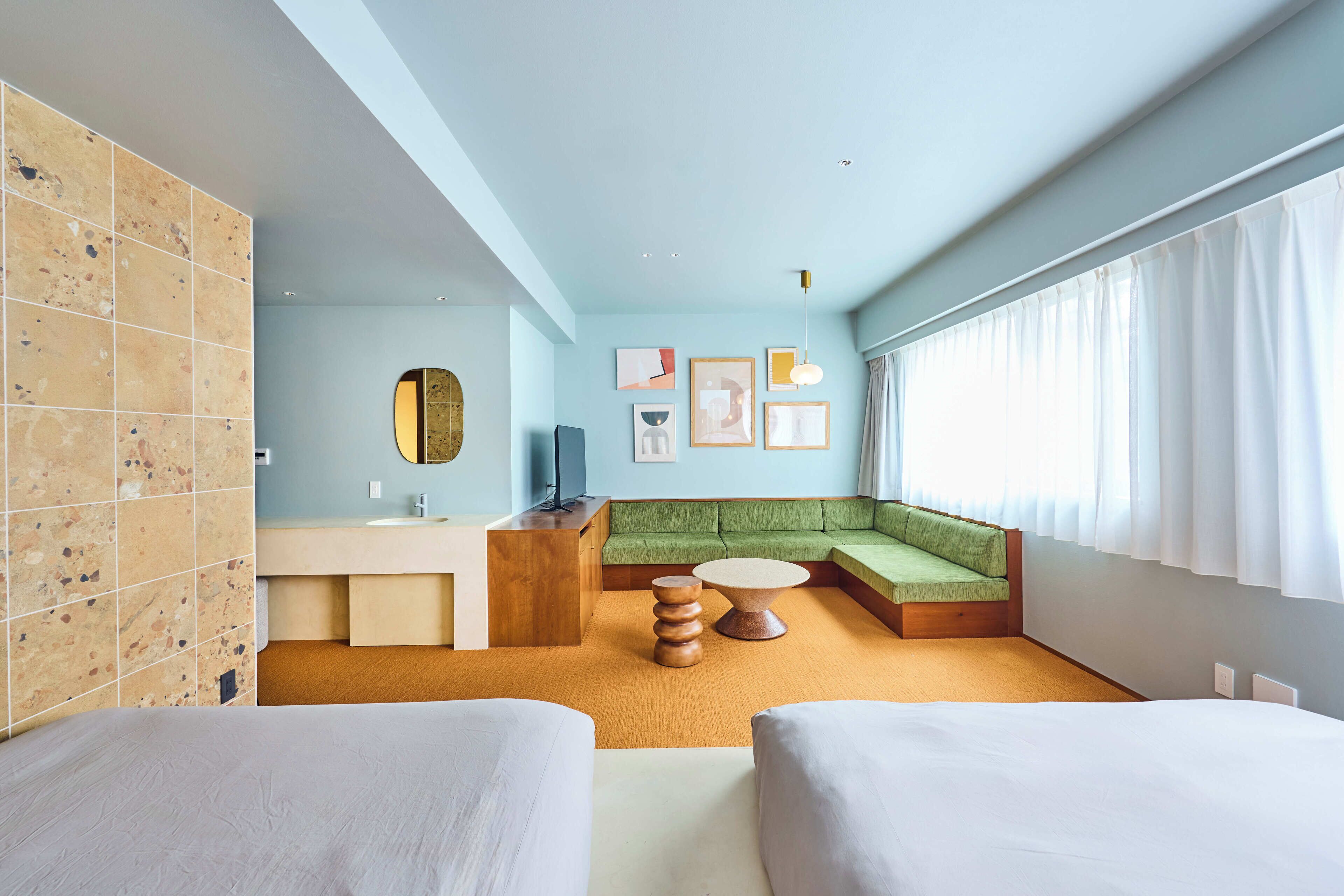 A modern hotel room with a green sofa, a round coffee table, and a large window with curtains.