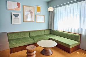 Una habitación con un sofá seccional verde, una mesa de centro redonda de madera y cuadros en la pared.