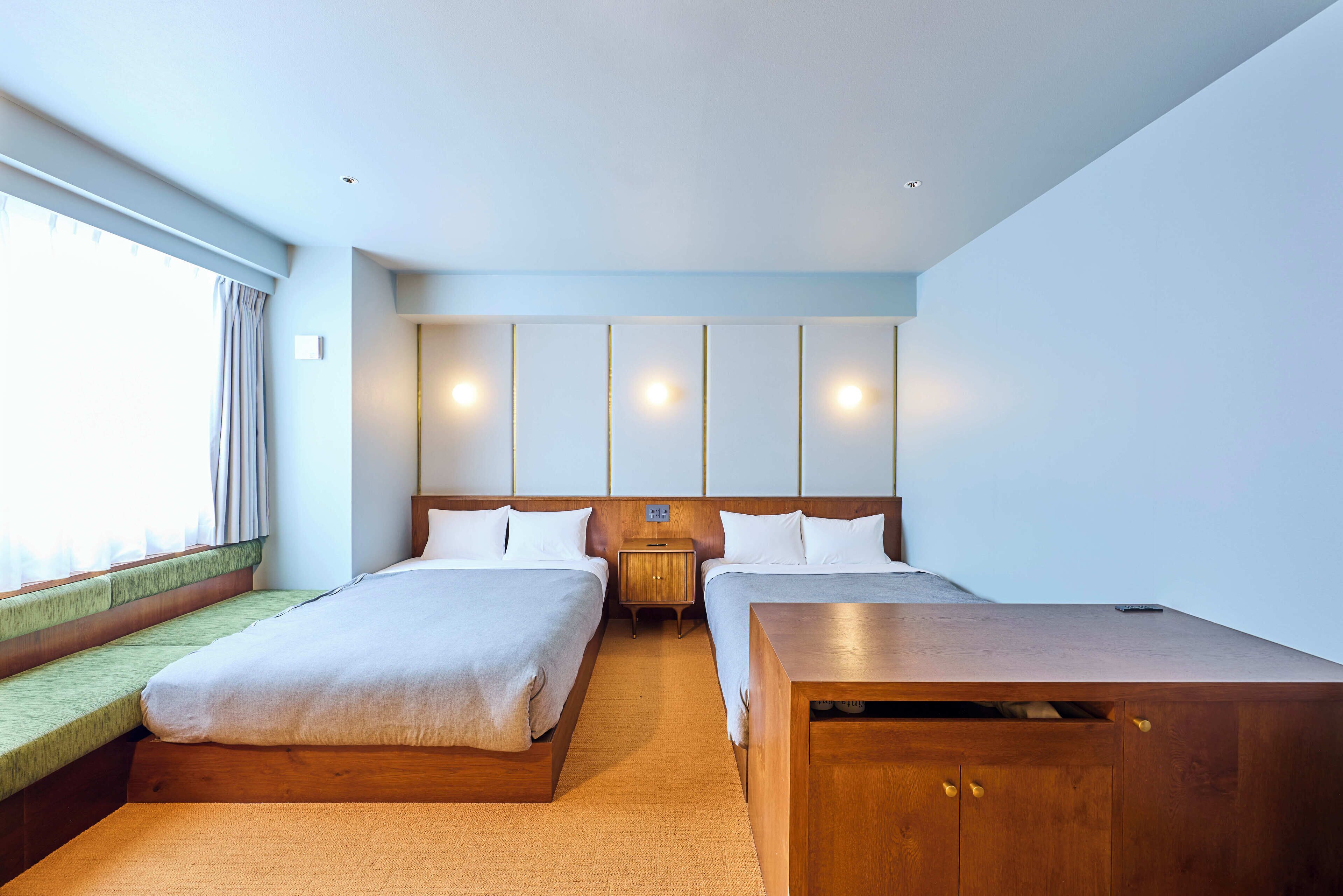 A hotel room with two beds, a wooden nightstand, and a desk.