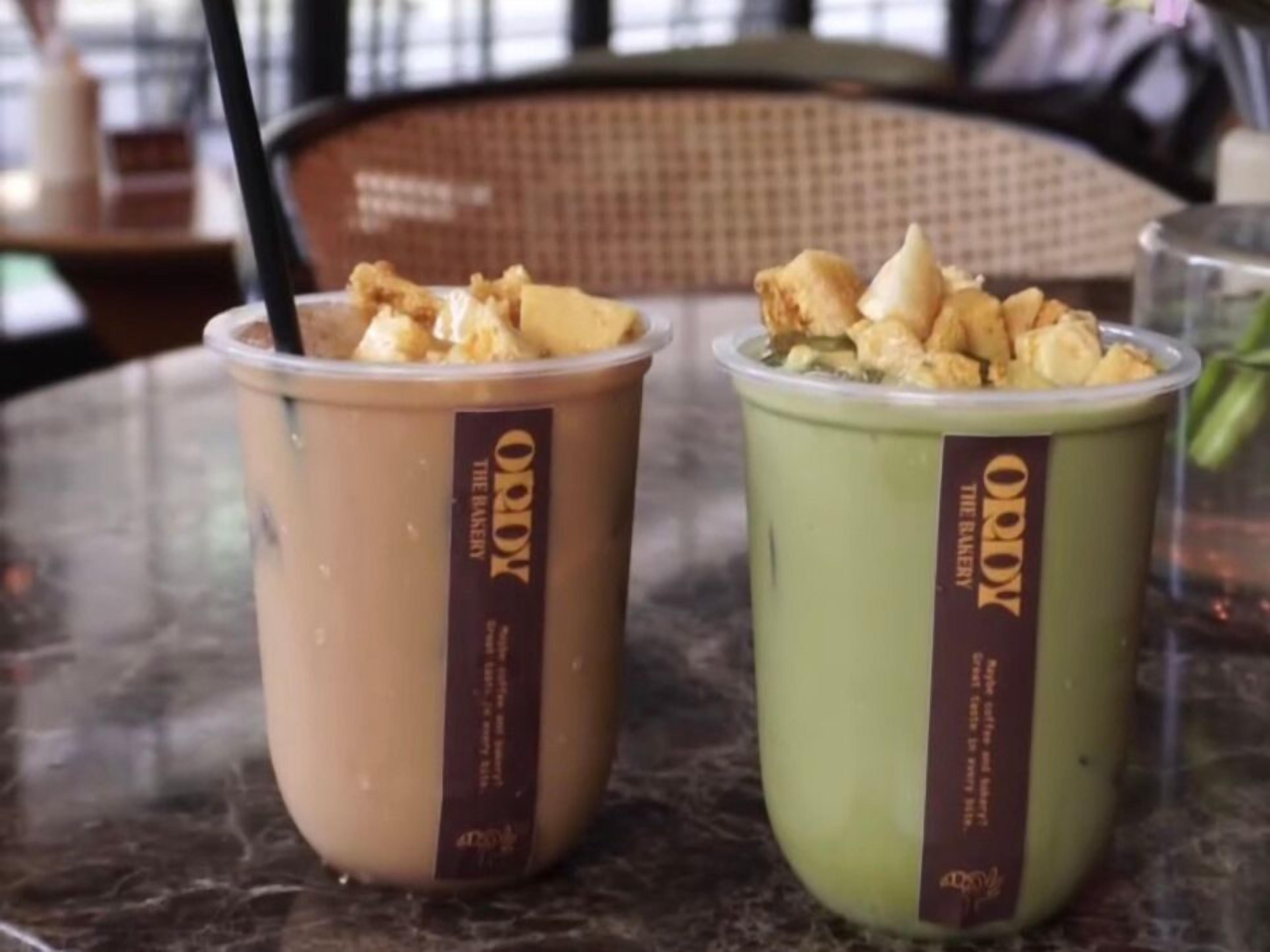Two cups of iced coffee with whipped cream and a straw, placed on a table.