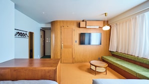 Habitación de hotel moderna con una pared de acento de madera, un televisor de pantalla plana, un banco acolchado verde y una mesa redonda.