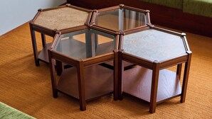 Un conjunto de cuatro mesas hexagonales de madera con tapas de vidrio, ubicadas sobre una alfombra naranja texturizada.