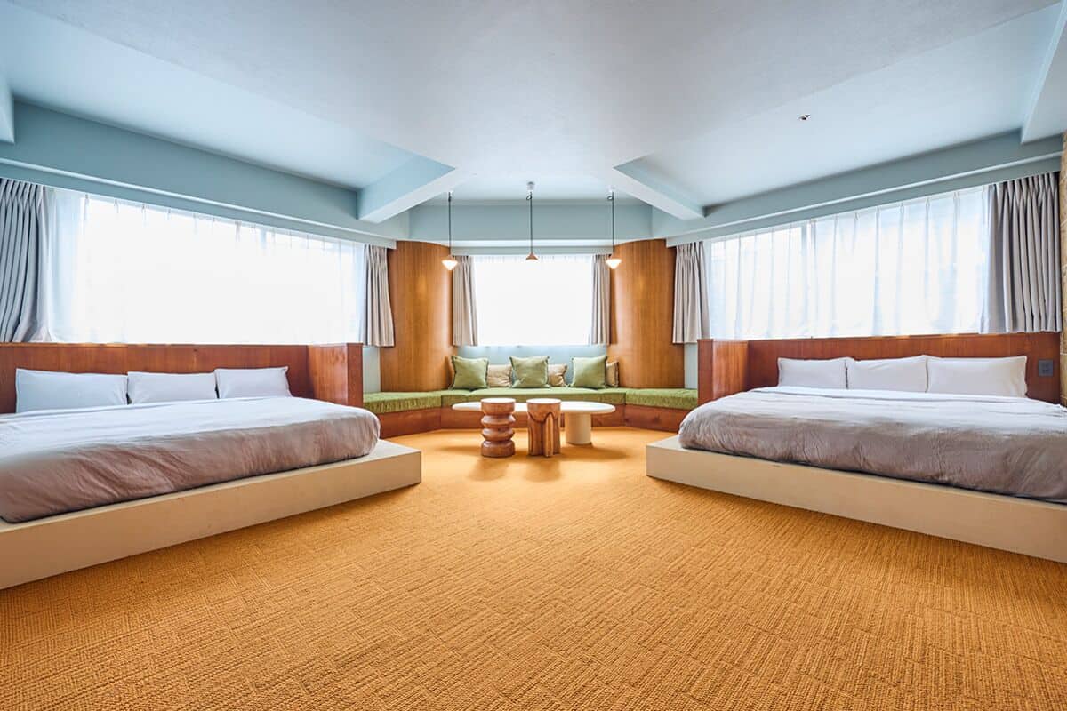 A hotel room with two beds, a seating area, and large windows.