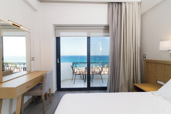 A hotel room with a bed, a desk, a chair, a balcony with a view of the sea, and a window with curtains. - Elegant Beach Hotel (Trifylia)
