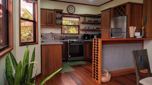Een kleine keuken met houten kastjes, een roestvrijstalen koelkast, een fornuis en een raam met uitzicht op groen.