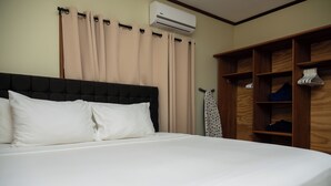 Een net opgemaakt bed met witte lakens, een donker hoofdbord en beige gordijnen.