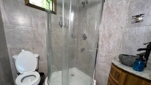 Een badkamer met een douche met glazen wand, een toilet en een wastafel met een stenen kom.