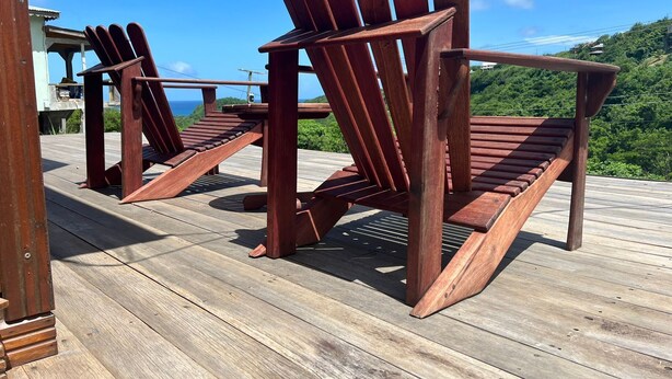Twee Adirondack stoelen op een houten terras met uitzicht op de oceaan en heuvels.