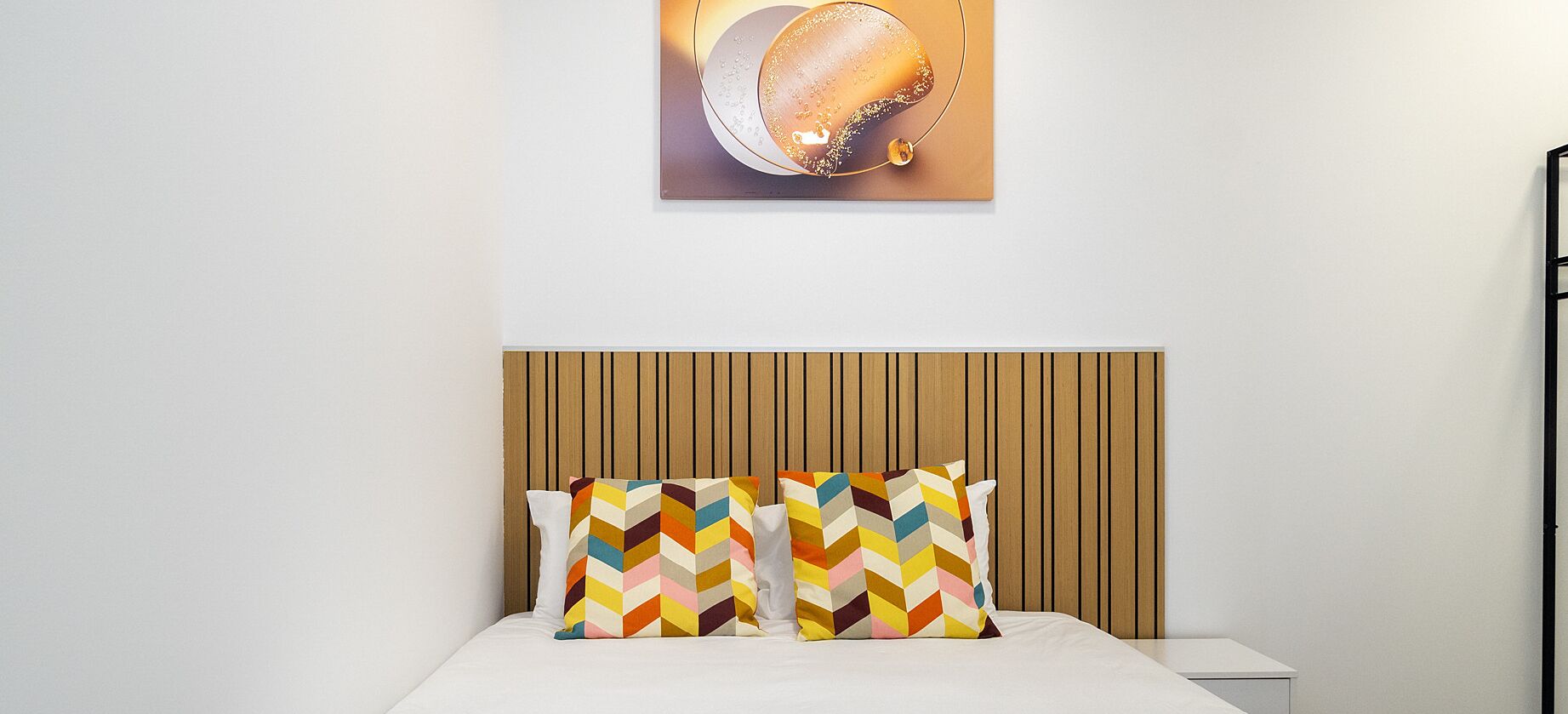 Una cama bien hecha con cabecera de madera y tres almohadas coloridas.