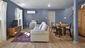 A living room with a sofa, a TV on a wooden cabinet, a dining table with chairs, and a patterned rug.