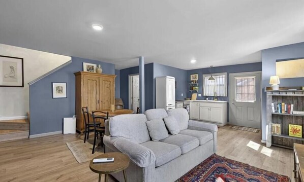 A living room with a sofa, a dining table, and chairs, a kitchen area with cabinets, and a bookshelf. - Quaint Mini Cottage in Shepherdstown - Walking Distance (Shepherdstown)