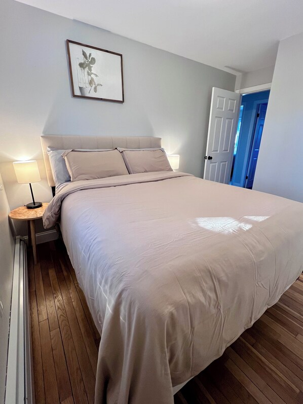A neatly made bed with a headboard, a bedside table with a lamp, and a framed picture on the wall. - 3-bedroom Cozy Home in Ellsworth with AC, WiFi (Ellsworth)