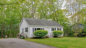 A single-story white house with a gabled roof, a front porch, and two small front yard bushes. - 3-bedroom Cozy Home in Ellsworth with AC, WiFi (Ellsworth)