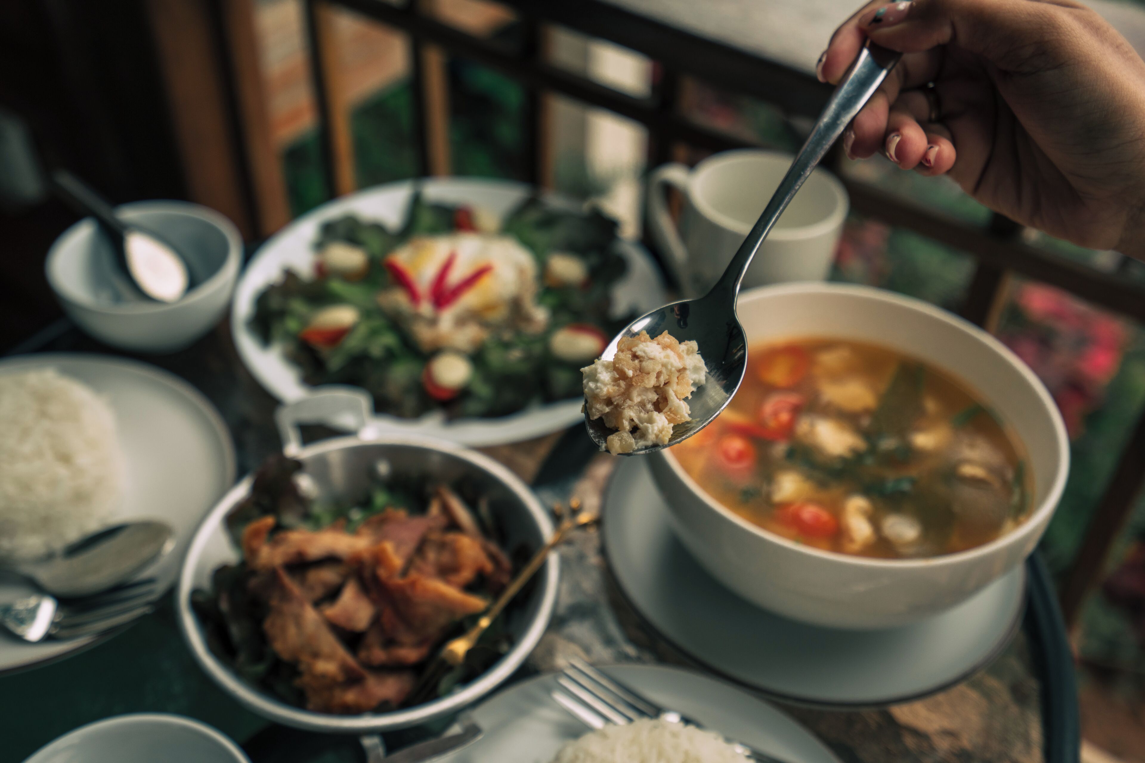 Una mesa de comedor con varios platos, incluyendo arroz, sopa y carne, y una cuchara en uso.