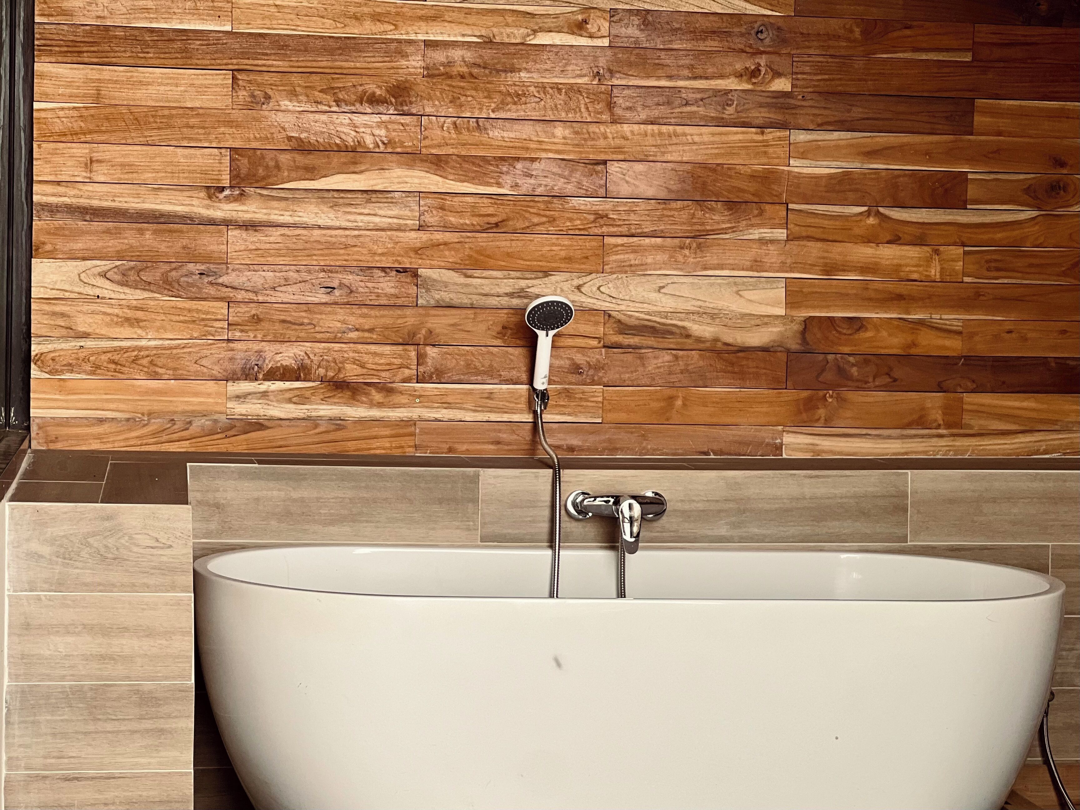 A bathtub with a shower head, set against a wooden wall with a tiled base.