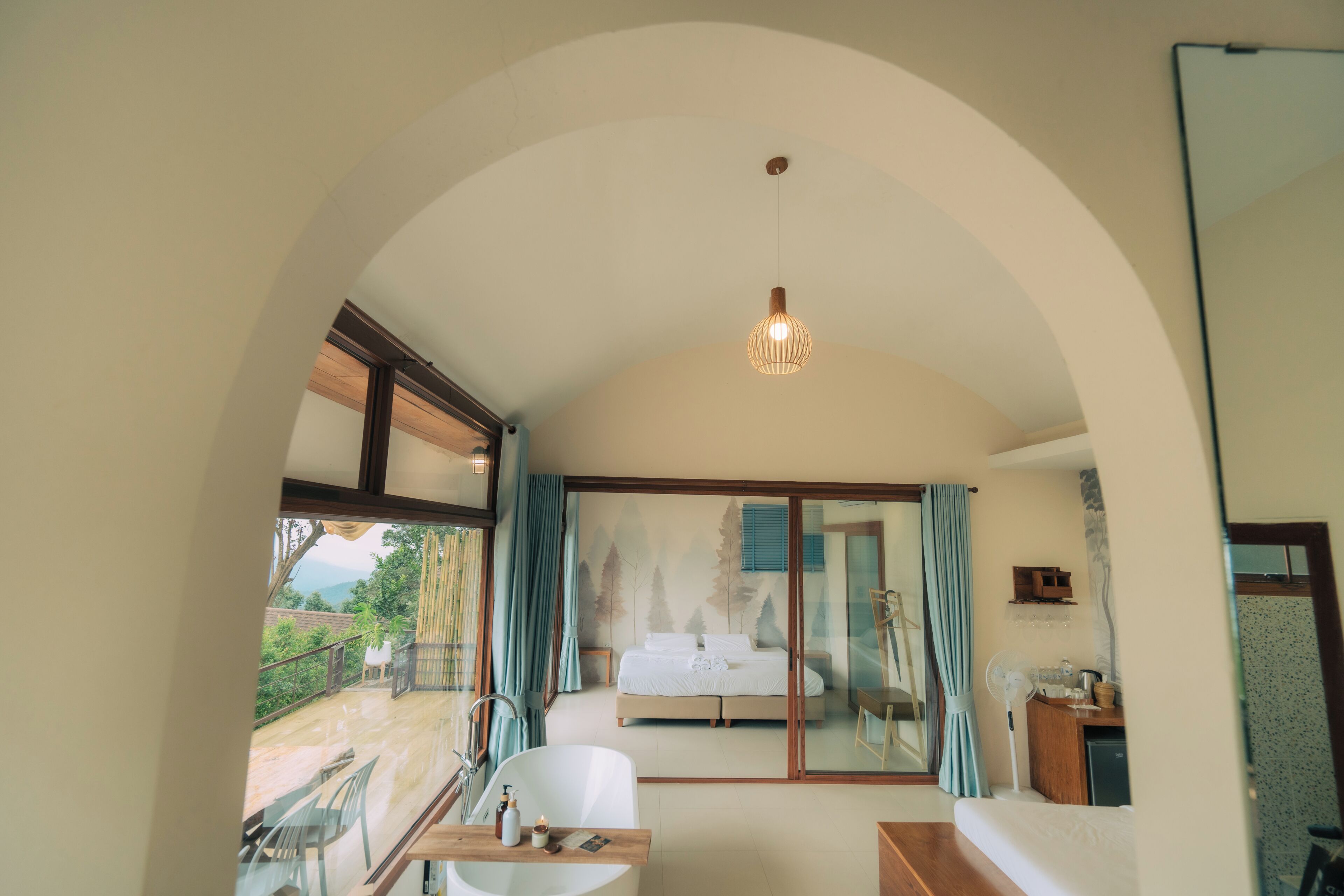 A bedroom with a bed, a desk, a chair, a mirror, and a view of the outdoors.