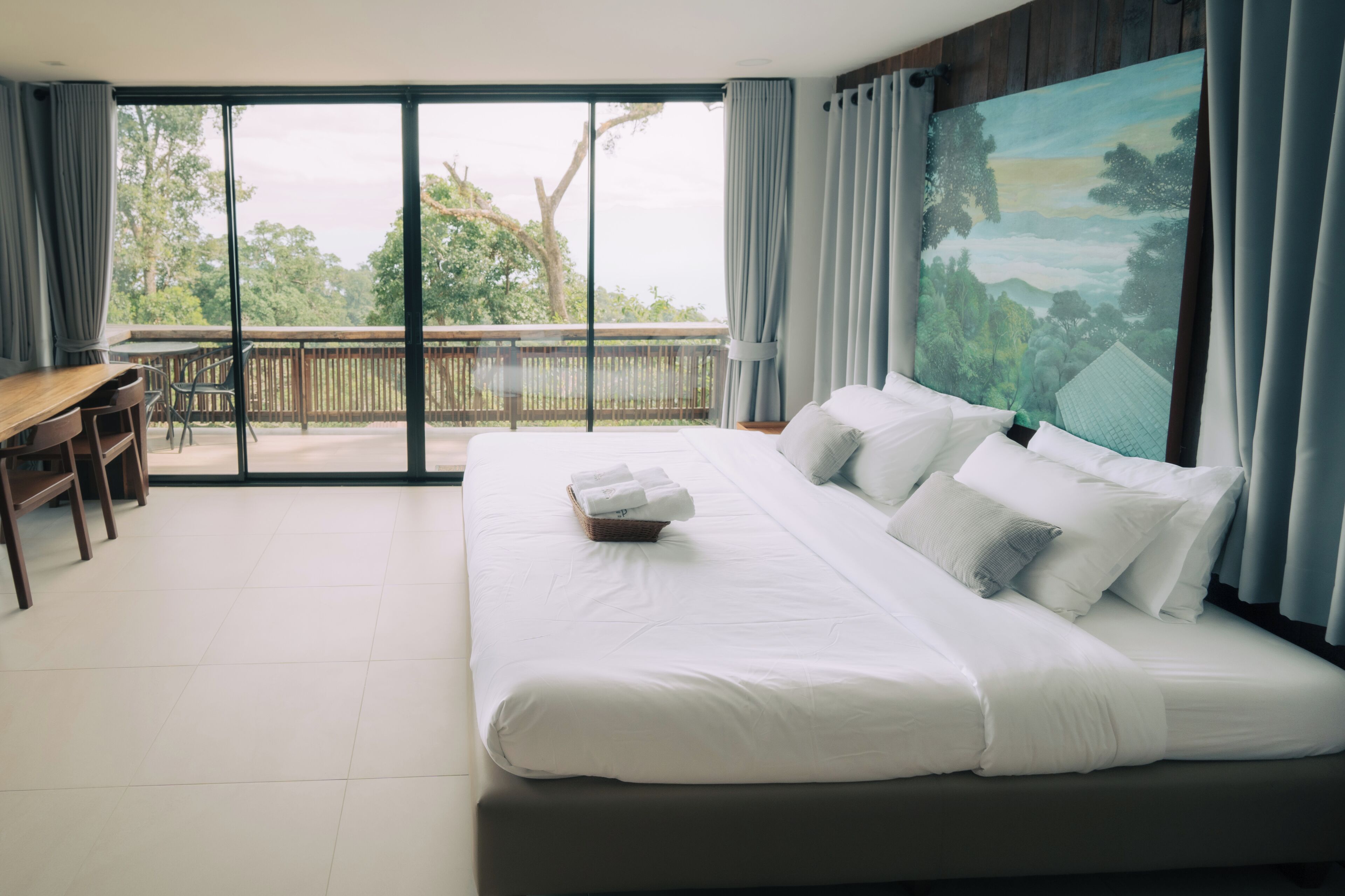 A hotel room with a large bed, a desk, and a balcony with a view of trees.