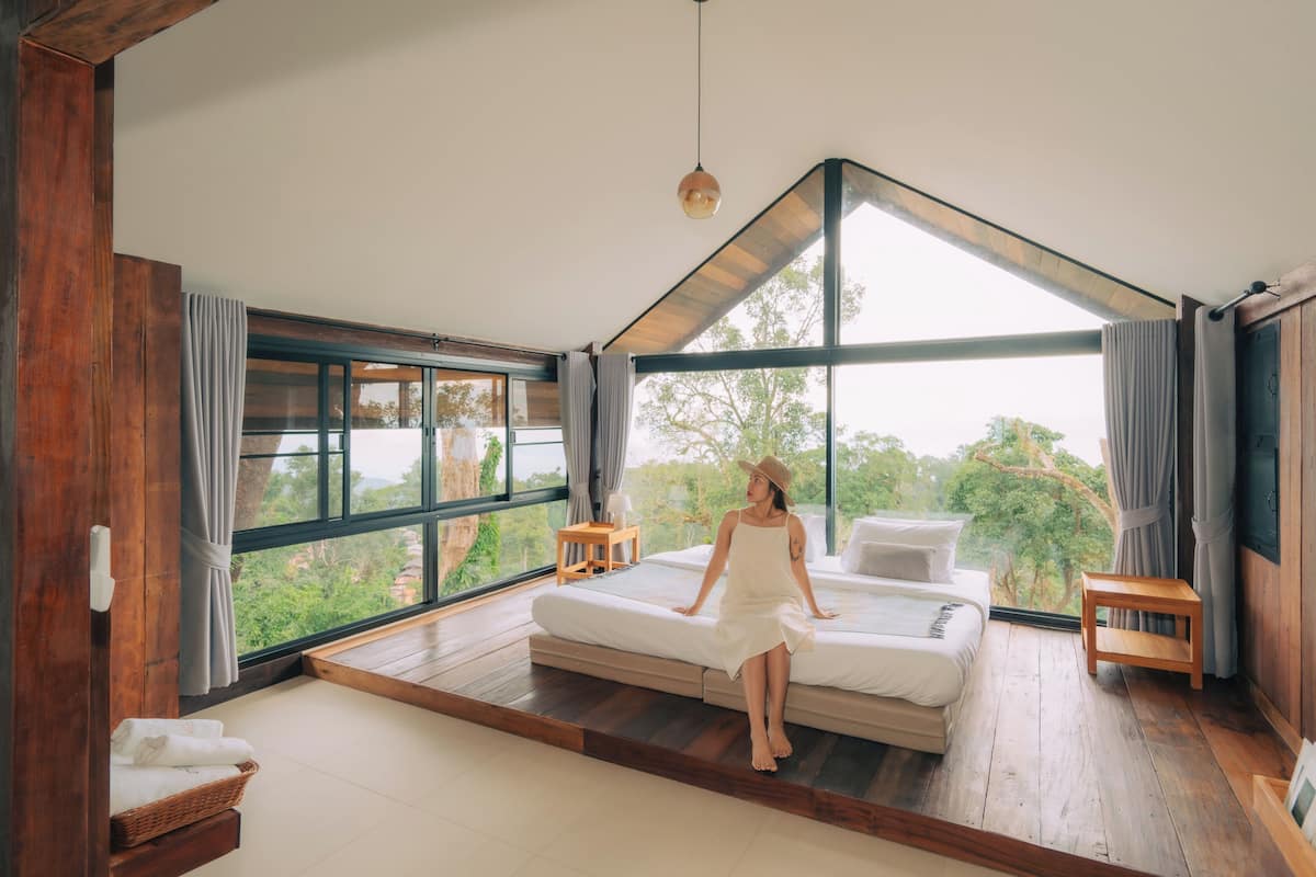 A spacious bedroom with a large window, a bed, a wooden floor, and a view of greenery.