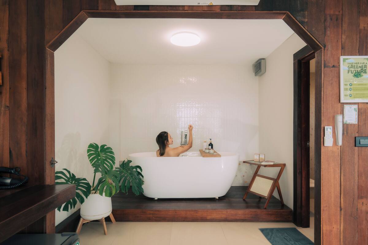 A bathroom with a freestanding bathtub, a potted plant, and a wooden bench.