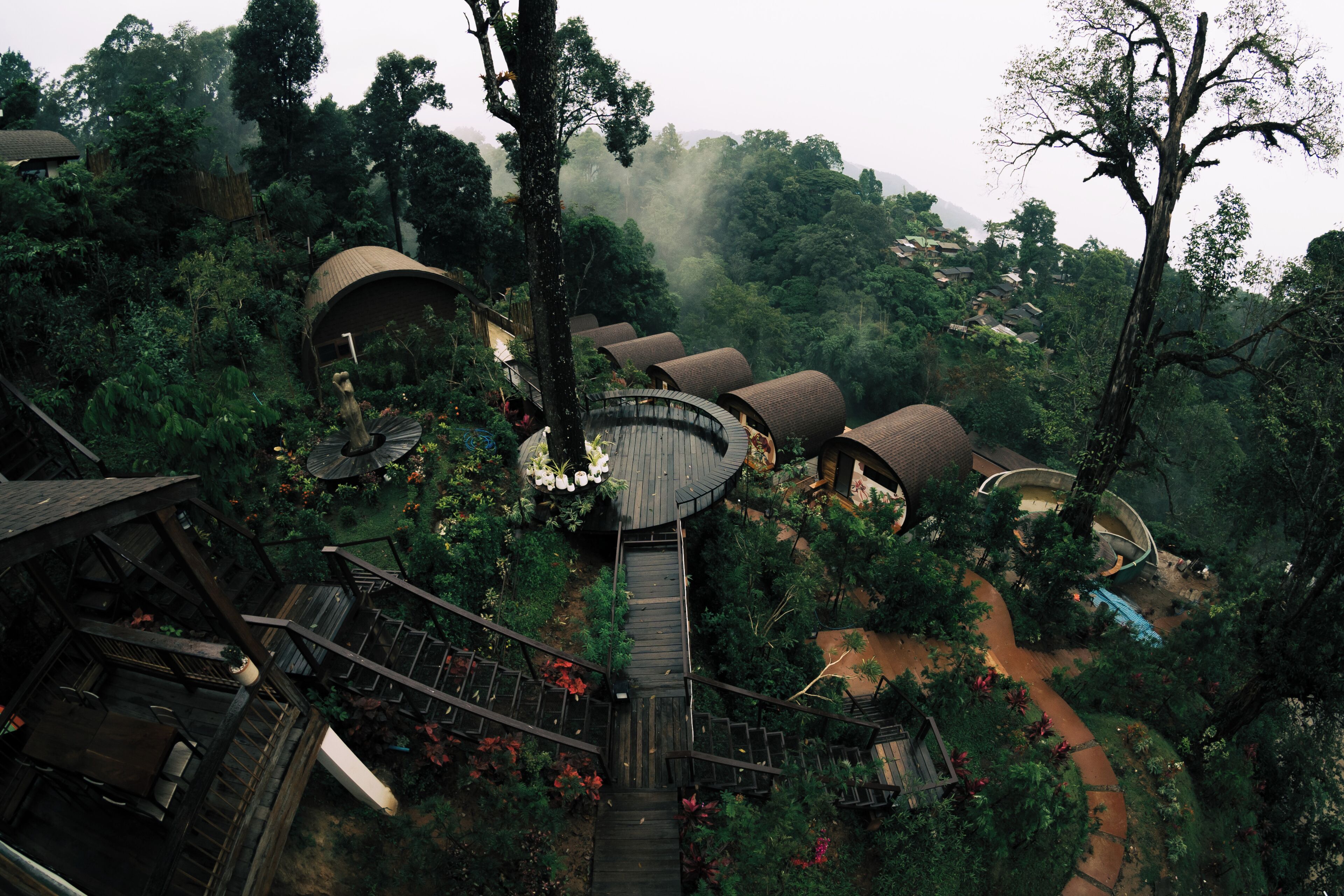 Un hotel árbol con varios niveles conectados por escaleras de madera, rodeado de exuberante vegetación y colinas boscosas.
