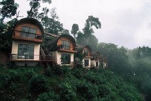 A row of modern, dome-shaped cabins nestled in a lush forest, each with a balcony and large windows. - Baan Nhuer Mek (Mae Taeng)