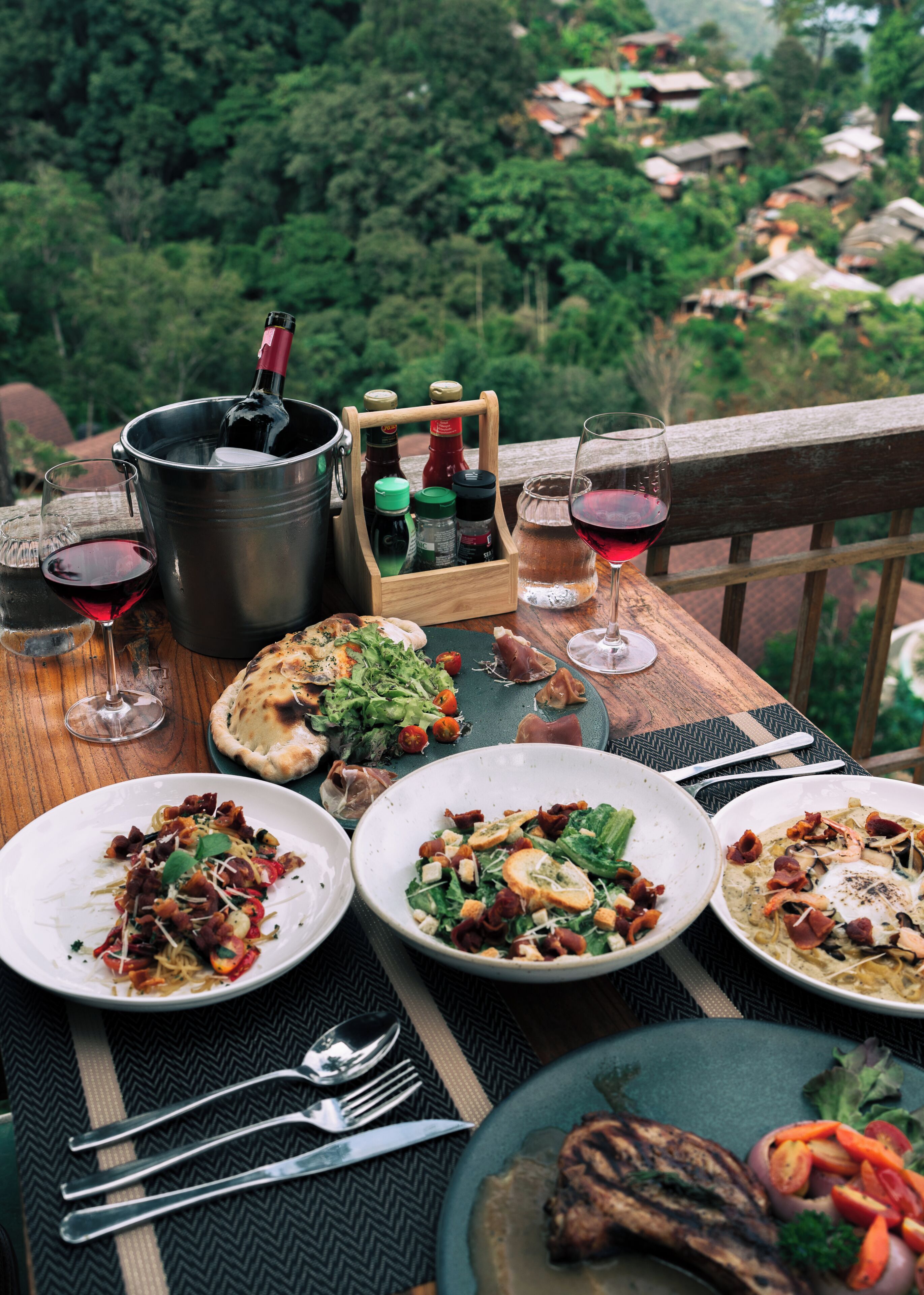 Una mesa servida con diferentes platos, copas de vino y una botella de vino.