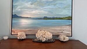 Ein gerahmtes Landschaftsbild mit ruhiger See und Bergen, präsentiert auf einem Holztisch zusammen mit drei dekorativen, korallenartigen Objekten.