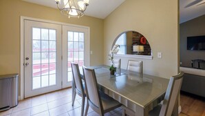 Un comedor con mesa y sillas, una araña y una cocina visible a través de un arco.