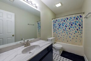 Un baño con un lavamanos blanco, un inodoro y una ducha con cortina de motivos azules y blancos.