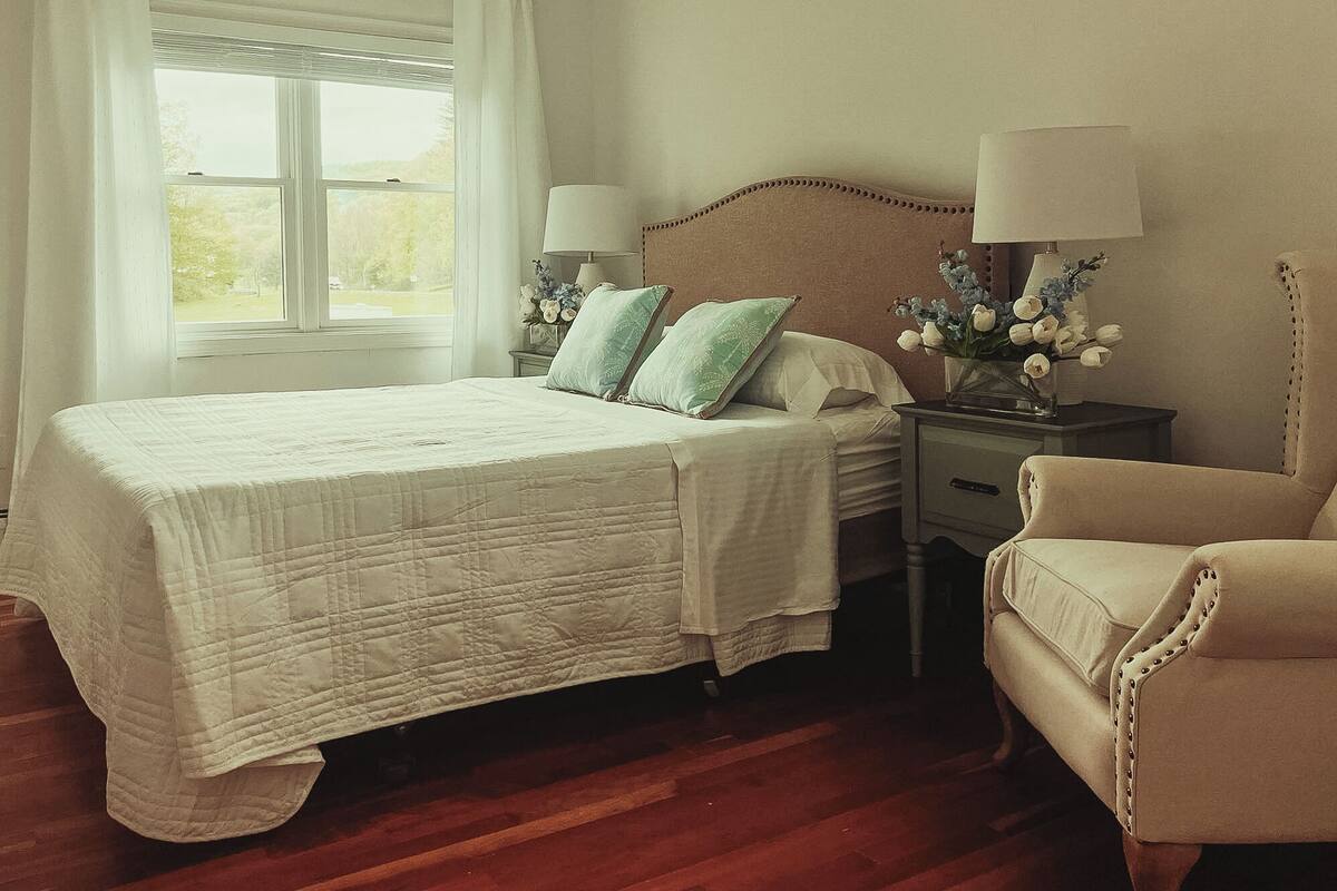 A bedroom with a bed, nightstands, a chair, and a window with curtains.