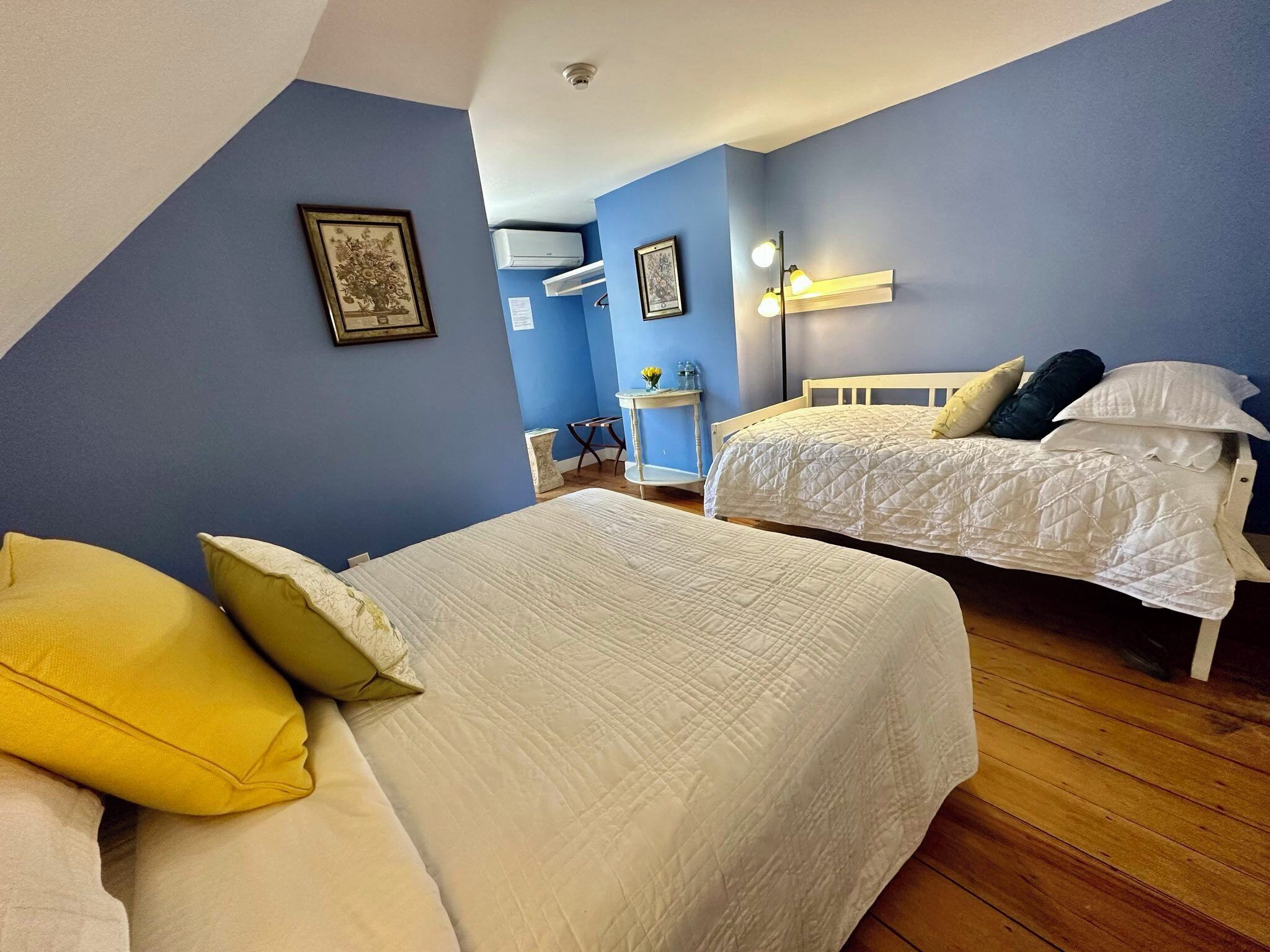 A bedroom with two beds, a desk, and an air conditioning unit.