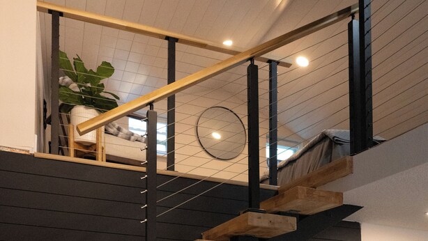 Una escala moderna amb graons de fusta i parets negres, un mirall rodó i una planta en test.