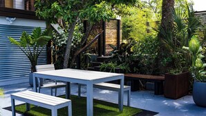 Un pati amb taula i bancs, envoltat de plantes diverses i una tanca de fusta.
