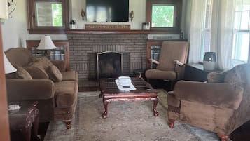 Una sala de estar con chimenea, dos sofás, una mesa de centro y un televisor sobre la chimenea.