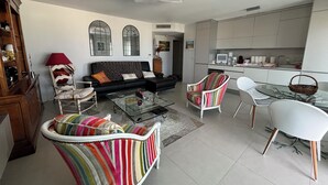 Una sala de estar moderna con un sofá, sillones a rayas, una mesa de centro de vidrio y un comedor con mesa y sillas de vidrio.