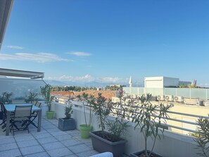 A rooftop terrace with a table and chairs, potted plants, and a view of a cityscape and mountains. - Apt 6 couchages/3 ch,7 min de la plage,5 min gare (Antibes)