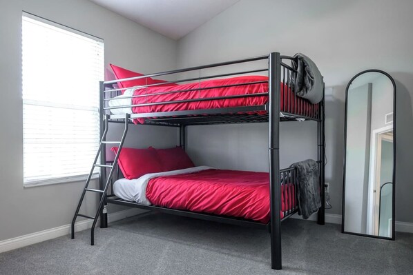 Una cama litera con ropa de cama roja, una escalera y un espejo en la pared.