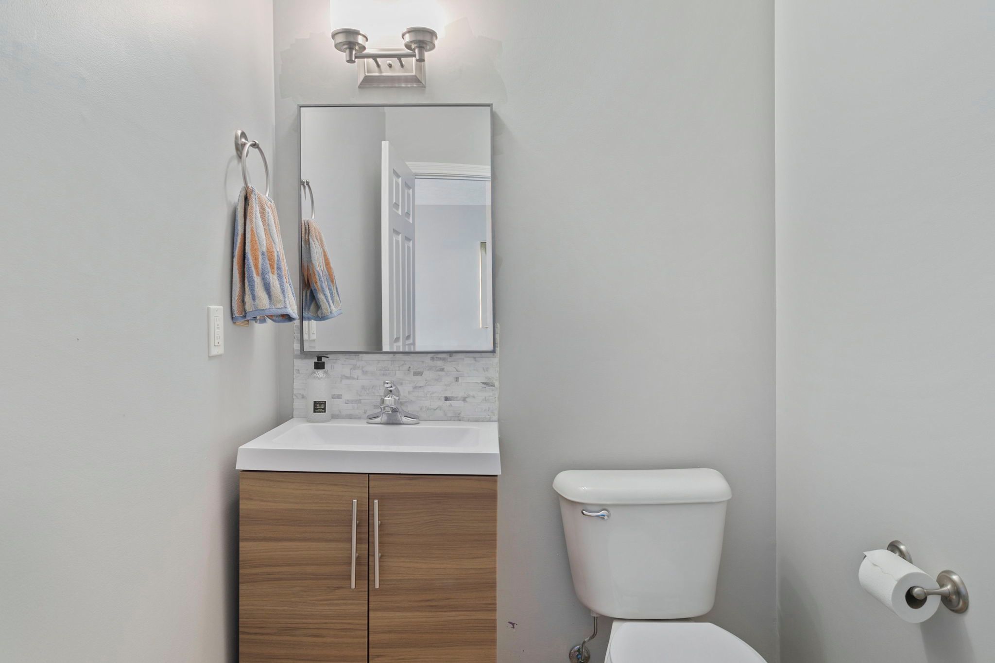 A bathroom with a white toilet, a sink with a mirror above it, and a towel hanging on a metal ring.