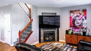 Una sala de estar con chimenea, una escalera y un cartel grande en la pared.