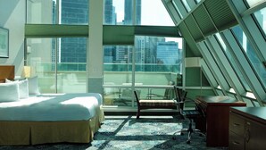Quarto de hotel moderno com uma cama grande, uma mesa e uma cadeira. Há vista da cidade através de amplas janelas.