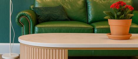 A green leather sofa with a potted plant, a white lamp, and a framed abstract painting on the wall.
