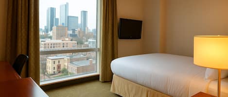 A hotel room with a bed, a desk, a lamp, and a TV on the wall.